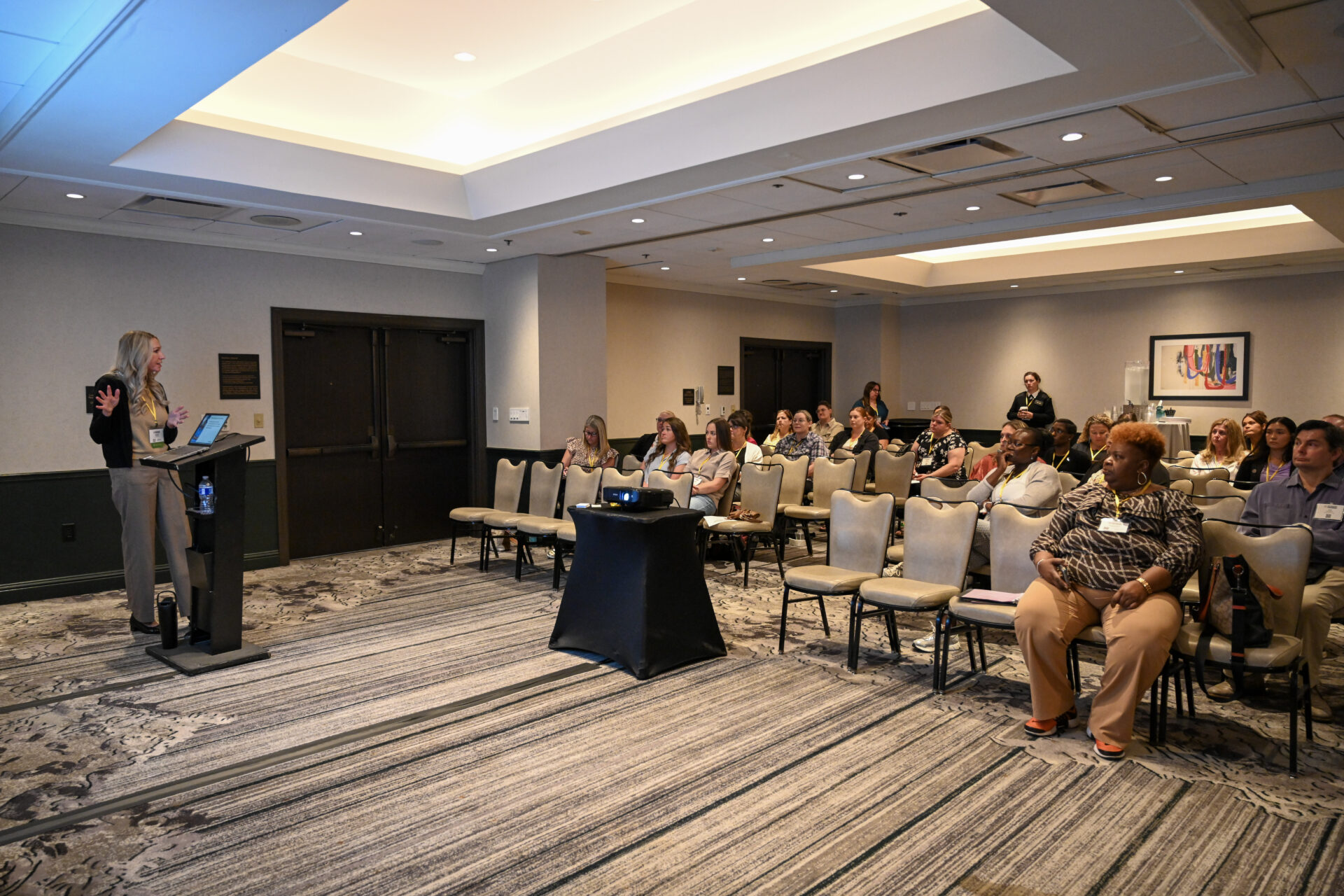 Woman presenting with a laptop to an attentive audience seated in a conference room.